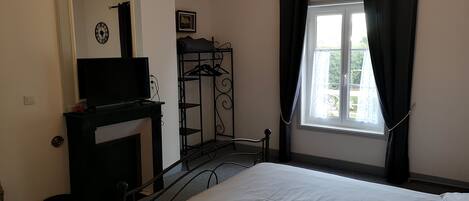 A bedroom with a bed, a television on a dresser, a chandelier, a window with curtains, and a coat rack.