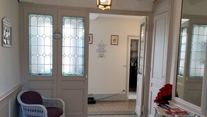 A hallway with patterned floor tiles, a white wicker chair, and a table with a vase of red flowers.