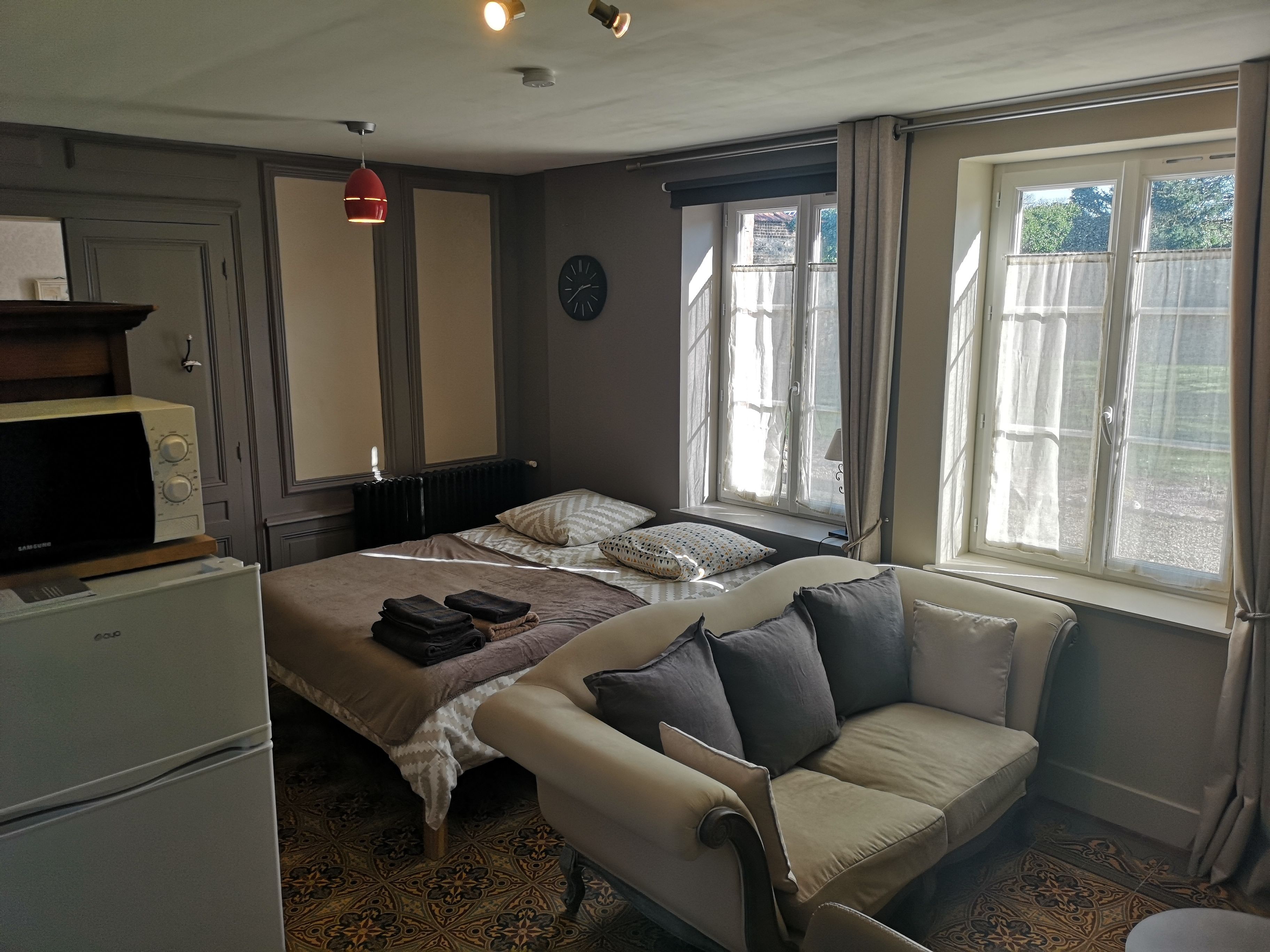 Une chambre à coucher avec un lit, un canapé, un radiateur, une horloge et une fenêtre avec des rideaux.