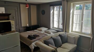 A bedroom with a bed, a sofa, a radiator, a clock, and a window with curtains.