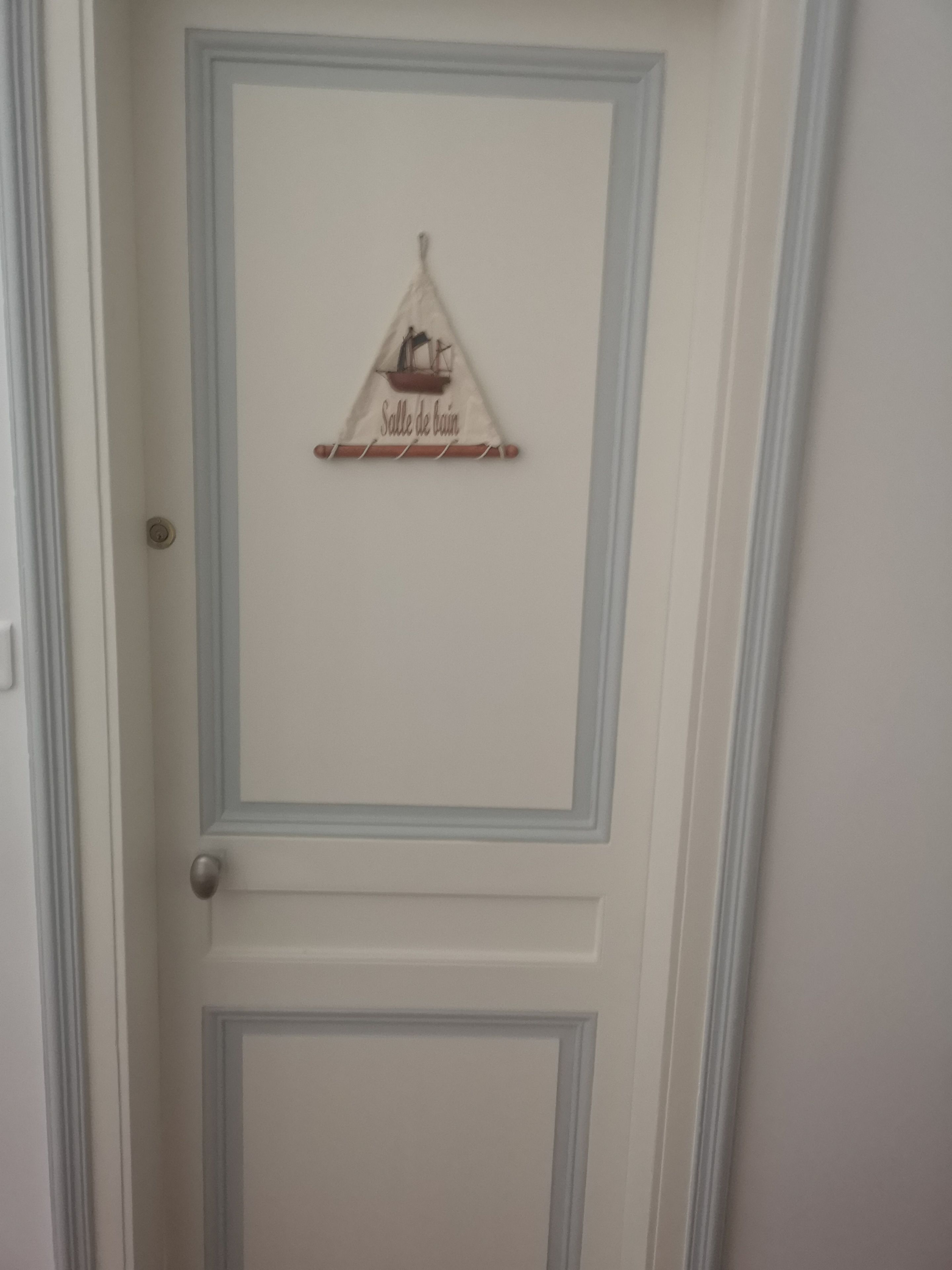 En vit dörr med en dekorativ skylt som visar texten ”Salle de Bain” (badrum).