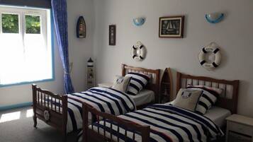 Quarto com duas camas de madeira, uma janela com cortinas azuis e decoração temática náutica.