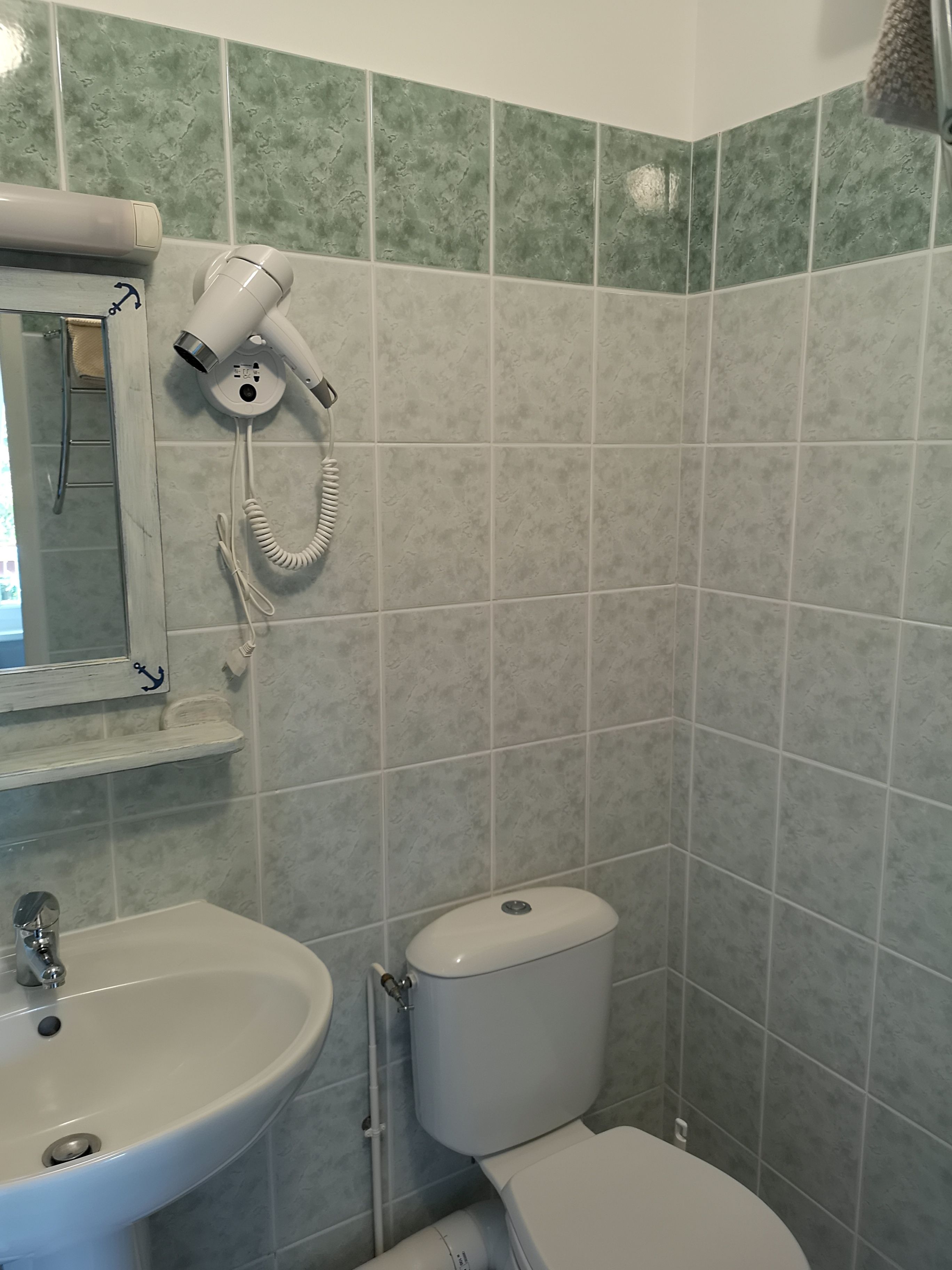 A bathroom with a sink, toilet, and hairdryer mounted on the wall.