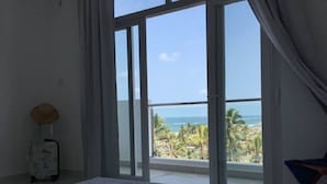 Et soveværelse med en stor skydedør, der fører ud til en balkon med udsigt over havet og palmer.