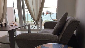 En moderne stue med sofa, et lille bord og havudsigt gennem store vinduer.