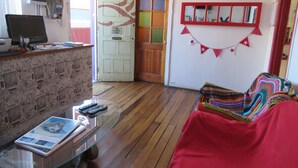 A room with a reception desk, a computer, a glass table with magazines, a red blanket, and a colorful knitted item. - Hostal Mirenart (Valparaiso)