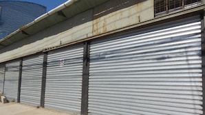 A row of closed metal roller doors with a security sign, a concrete floor, and a metal roof. - Hostal Mirenart (Valparaiso)