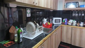 A kitchen with wooden cabinets, a dish rack, a microwave, and various kitchen items on the counter. - Hostal Mirenart (Valparaiso)