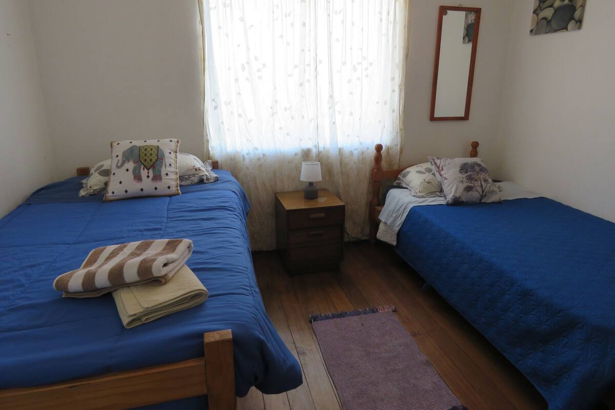 Quarto com duas camas, mesa de cabeceira, espelho e janela com cortinas.