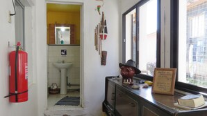 A narrow hallway with a wooden floor, a fire extinguisher, a sink, and a window with a view of buildings outside. - Hostal Mirenart (Valparaiso)