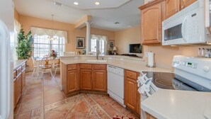 A spacious kitchen with wooden cabinets, a large island, white appliances, and a dining area with chairs and a table. - Magical Villa with pool and spa in quiet community (Davenport)