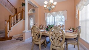 A dining room with a wooden staircase, a chandelier, and a large window with curtains. - Magical Villa with pool and spa in quiet community (Davenport)