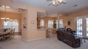 A spacious living room with a brown leather sofa, a dining area with wooden chairs, and a kitchen in the background. - Magical Villa with pool and spa in quiet community (Davenport)