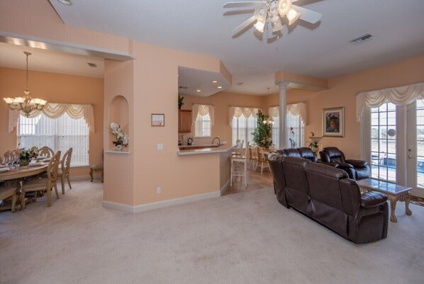 A spacious living room with a brown leather sofa, a dining area with wooden chairs, and a kitchen in the background.