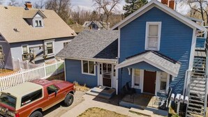 Una casa de dos pisos con fachada azul, un porche delantero y una camioneta roja estacionada en la entrada.