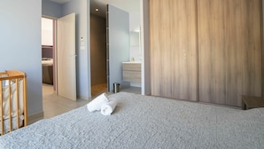 A modern hotel room with a large bed, a wooden wardrobe, a bathroom with a mirror, and a small wooden table.