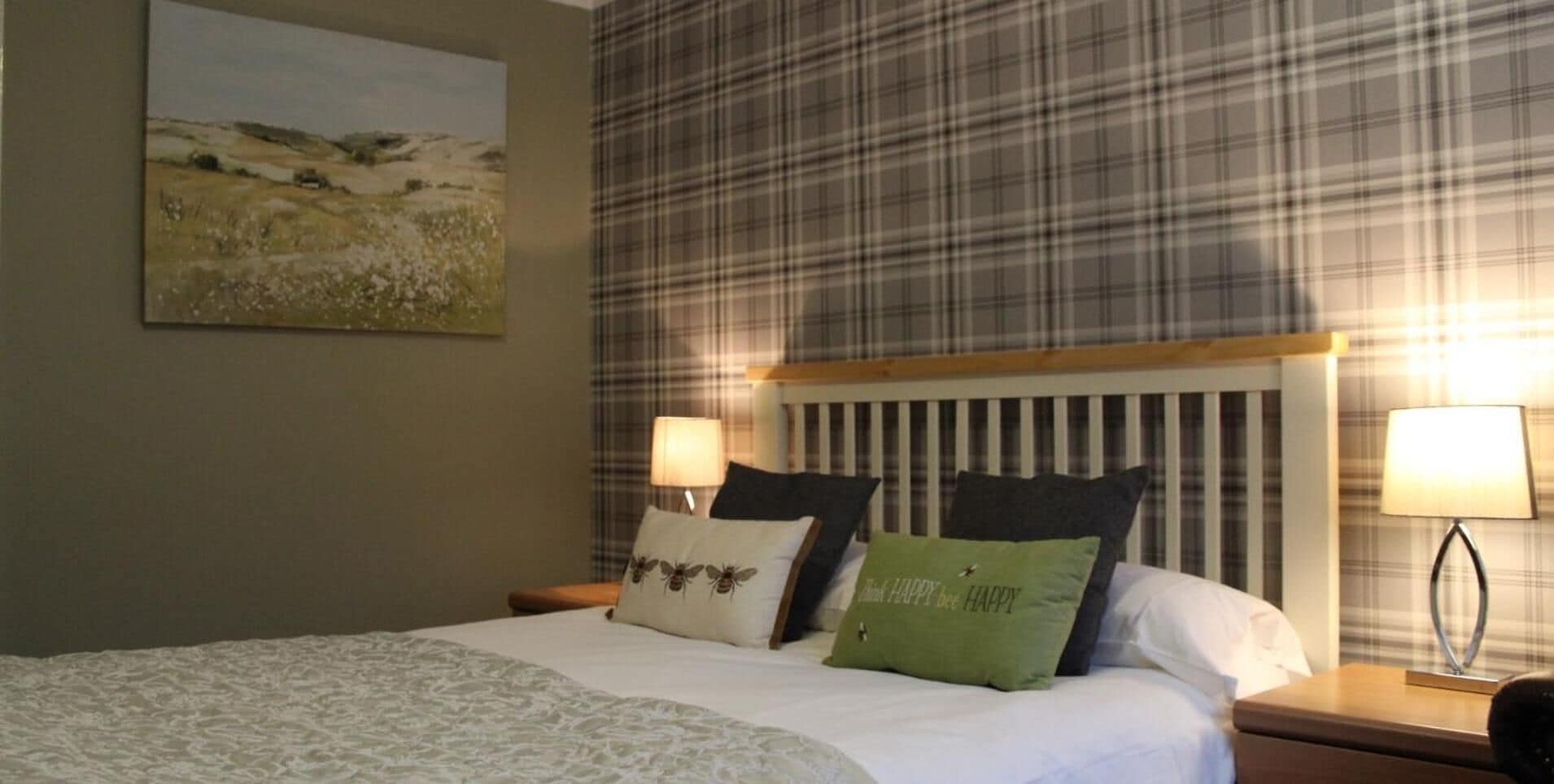 A hotel room with a bed, a headboard, a nightstand, a lamp, and a painting on the wall.