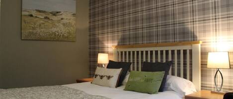 A hotel room with a bed, a headboard, a nightstand, a lamp, and a painting on the wall.