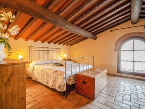 A rustic bedroom with a wooden ceiling, a bed with a metal frame, a bedside table, a nightstand, and a window with a view.