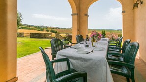 Un espacio comedor al aire libre cubierto, con una mesa dispuesta para seis personas, rodeado de sillas verdes, con vistas a un paisaje pintoresco.
