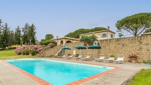 Una piscina rectangular con un muro de piedra y escalones que llevan a un edificio.