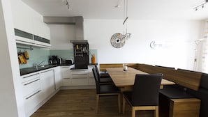 Moderni keittiö, jossa on valkoiset kaapit, puinen ruokapöytä ja mustat tuolit.