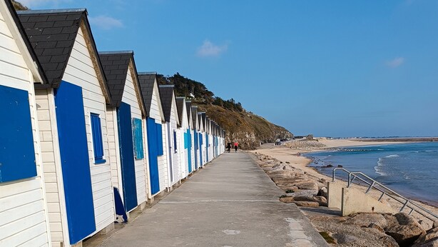 A row of beach huts with a concrete walkway leading to the sea.
