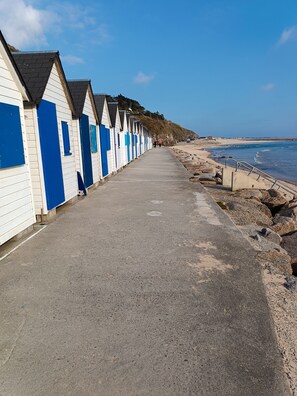 En rad strandhytter med en gångbana av betong som leder ner till havet.