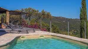 Une piscine d’un bleu éclatant, bordée de chaises longues et entourée de dalles de pierre et d’une pergola.