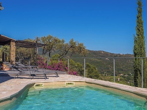 A clear blue pool with lounge chairs, surrounded by stone tiles and a pergola.