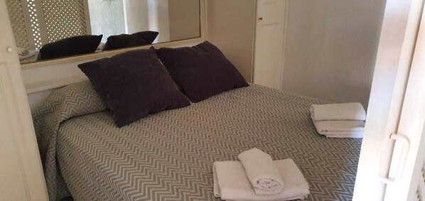 Un lit bien fait, avec une couvre-lit à motifs, deux oreillers foncés et des serviettes pliées posées sur le côté.