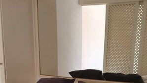 Una cama bien hecha con una colcha estampada, dos almohadas oscuras y una toalla blanca enrollada al lado.