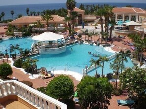 Une grande piscine extérieure entourée de palmiers et de chaises longues, avec une vue sur l’océan en arrière-plan.