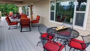 A covered outdoor patio with a round table and chairs, a dining table with chairs, and a large window offering a view of greenery.