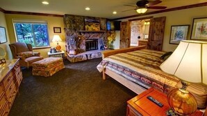 A bedroom with a large bed, a fireplace, a chair, a dresser, and a lamp.