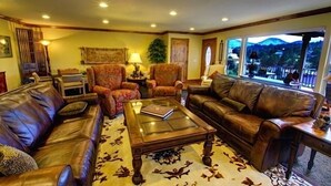 A living room with leather sofas, a glass coffee table, and a view of mountains through large windows.