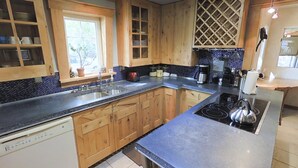 Une cuisine avec des meubles en bois, un plan de travail noir, une cuisinière encastrée et une fenêtre agrémentée d’une plante.