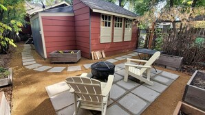 Un jardin avec un abri de jardin rouge, un foyer, deux fauteuils Adirondack et un parterre.