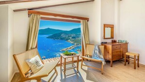 A room with a balcony overlooking a coastal view, wooden furniture, and a wooden dresser. - Secluded & Luxurious Mediterranean Villa w/ Heated Infinity Pool & Kids' Pool (Kalkan)