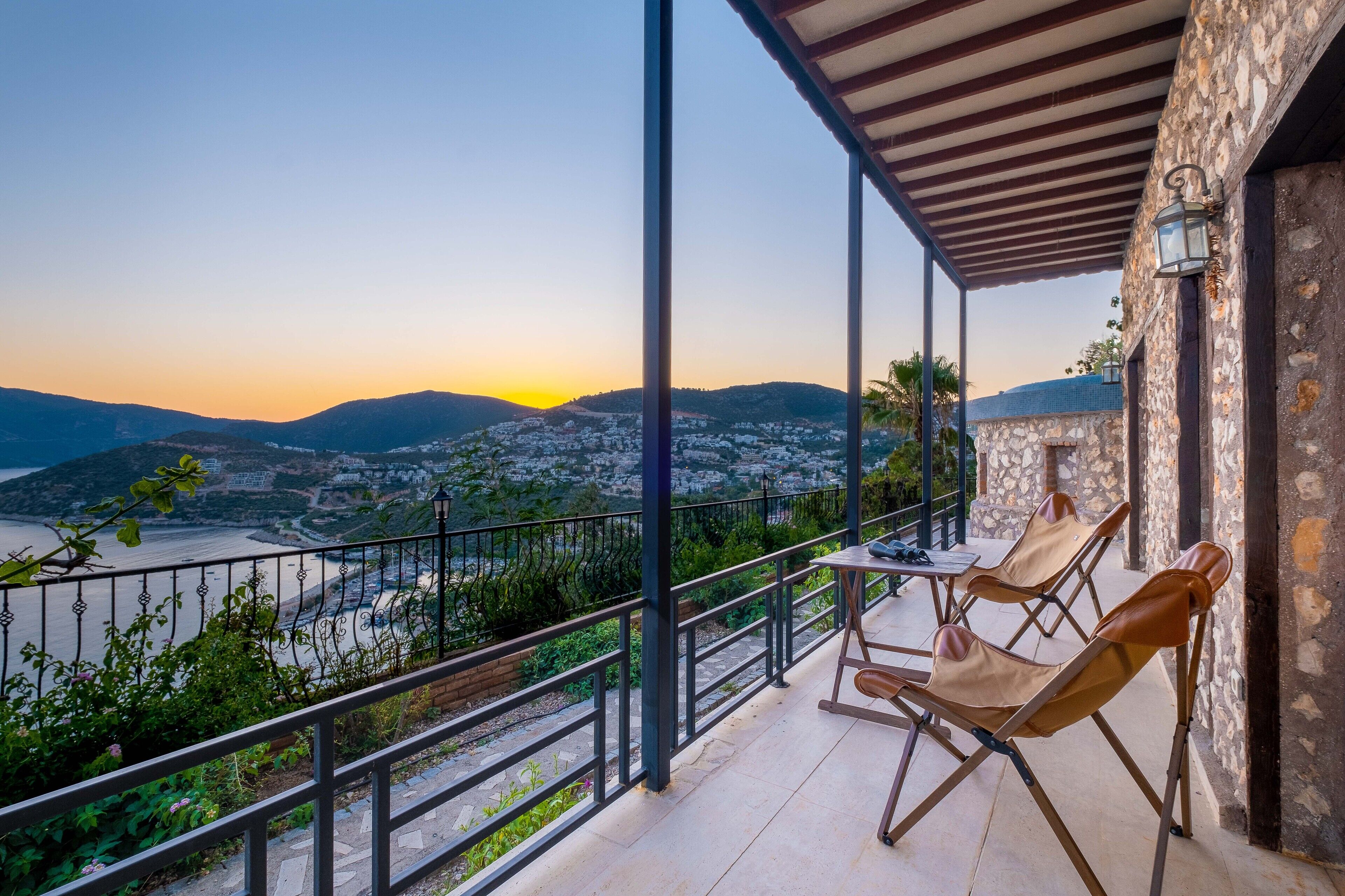 A balcony with a view of a coastal town and mountains at sunset.