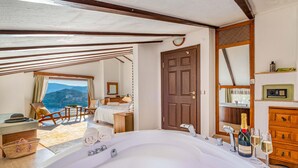 A spacious bedroom with a large bed, a view of the mountains, a wooden door, and a bathroom with a bathtub and champagne. - Secluded & Luxurious Mediterranean Villa w/ Heated Infinity Pool & Kids' Pool (Kalkan)