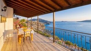 A covered terrace with a table and chairs, overlooking a coastal town and the sea. - Secluded & Luxurious Mediterranean Villa w/ Heated Infinity Pool & Kids' Pool (Kalkan)