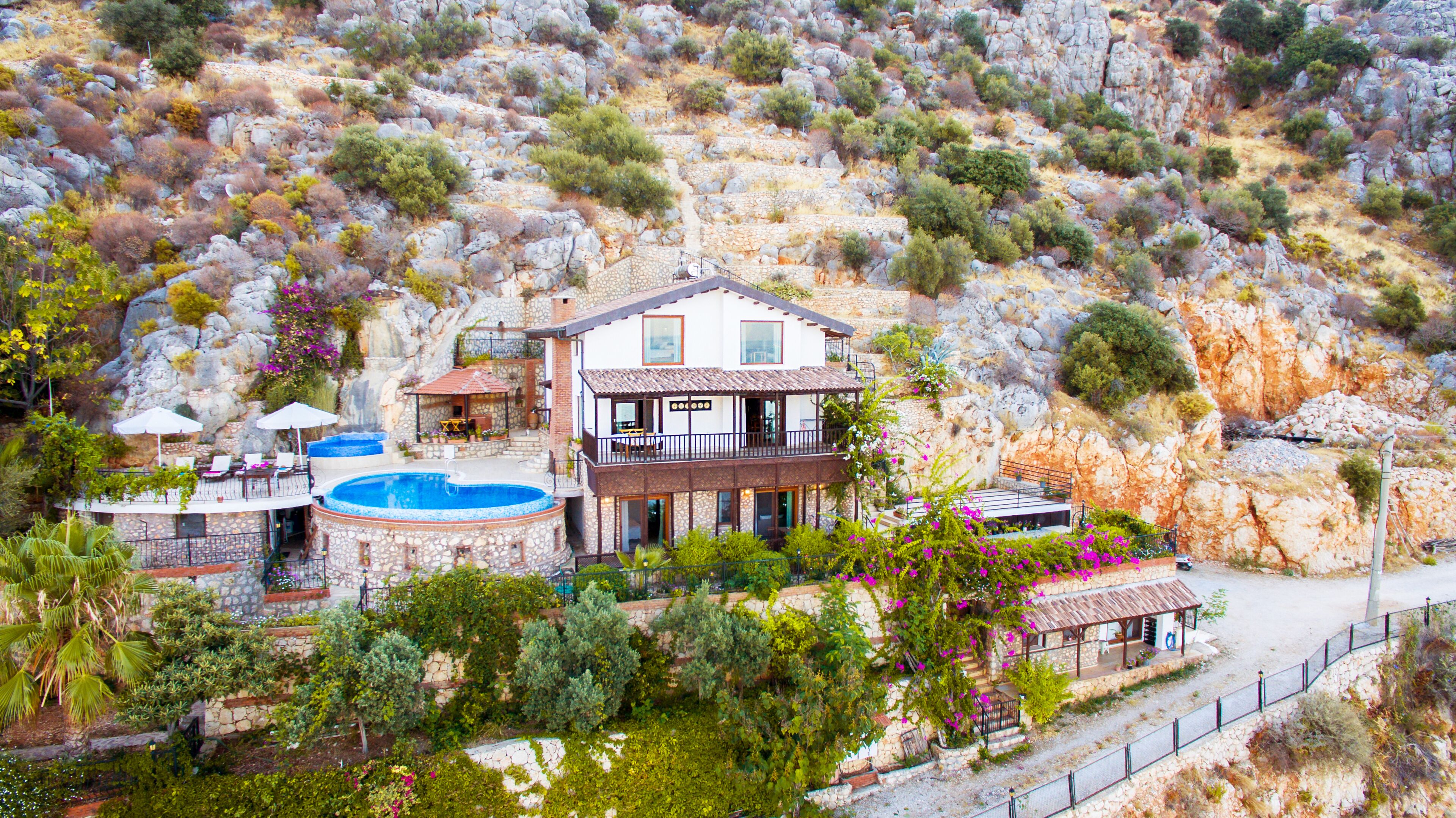 Ein zweistöckiges Haus mit Swimmingpool, Terrasse und Blick auf die umliegende felsige Landschaft.
