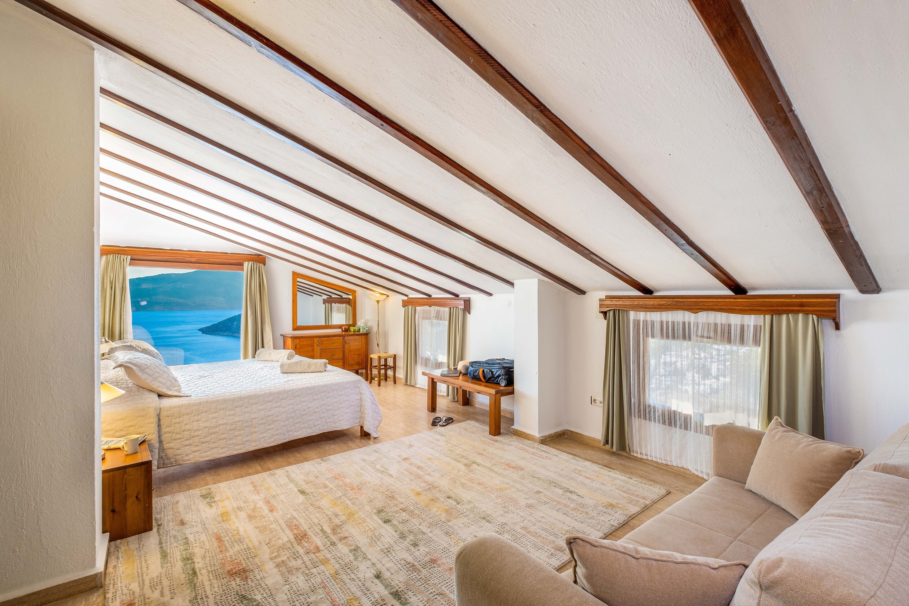 Un dormitorio espacioso con una cama grande, una zona de estar con sofá, un escritorio y vista al océano.