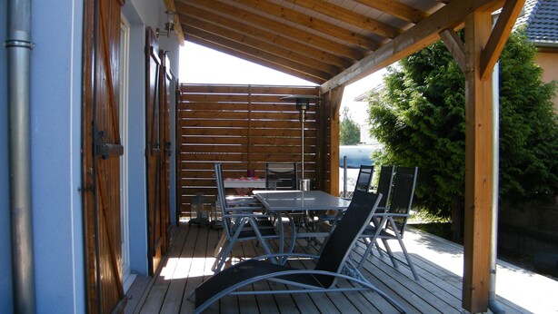 Une terrasse extérieure avec une plateforme en bois, une table et des chaises, ainsi qu’un barbecue.