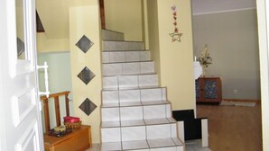 Un escalier recouvert de carreaux blancs, avec une main courante en bois et une petite table en bois ornée d’une bougie et d’objets décoratifs.