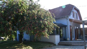 Une maison avec une allée en gravier, un grand arbre aux baies rouges et un patio abrité.