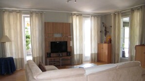 Un salon avec un canapé blanc, un téléviseur posé sur un meuble en bois et une armoire.