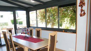 Un coin repas avec une table en bois, des chaises et une vue sur les arbres à travers de grandes fenêtres.