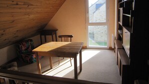 A room with a sloped ceiling, a wooden table, two chairs, a bookshelf, and a door leading outside.